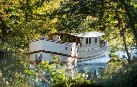 Cream-and-white river barge gliding along a tree-shaded waterway