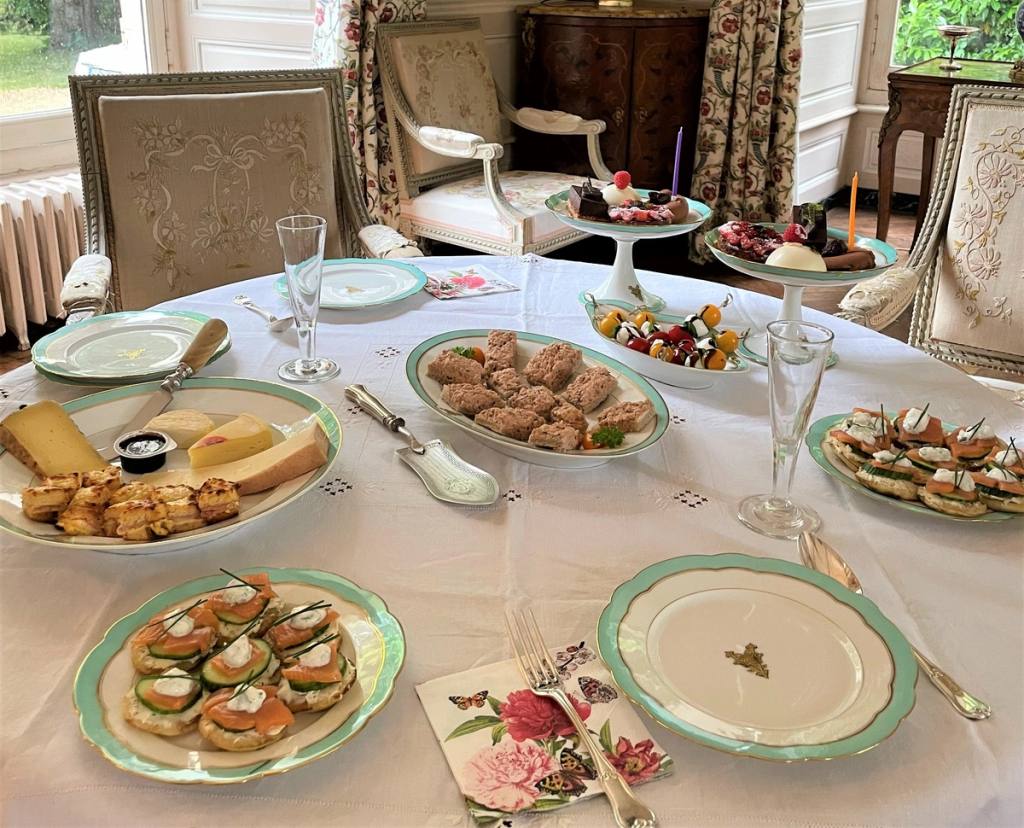High tea spread of savoury canapés, sandwiches, cheese and cakes on a white embroidered tablecloth
