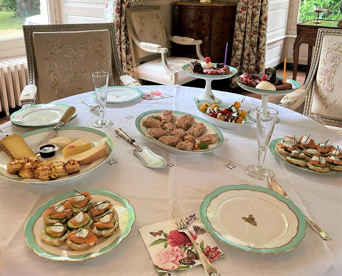 Buffet de high tea : canapés salés, sandwichs, fromage et gâteaux sur une nappe blanche brodée