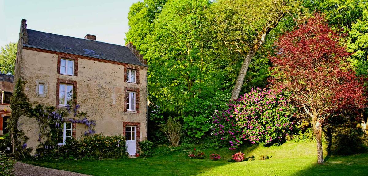 Cottage Les Glycines: stone house with wisteria, beside tall trees and flowering rhododendrons