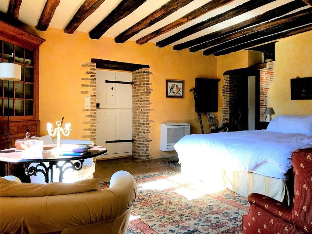 Cottage Les Glycines bedroom: exposed beams, ochre walls, brick-framed door and a large white bed