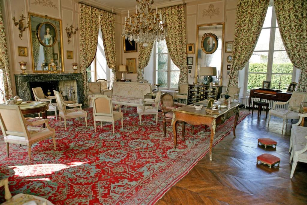 Grand Salon with crystal chandelier, family portraits, flat desk and red carpet on parquet