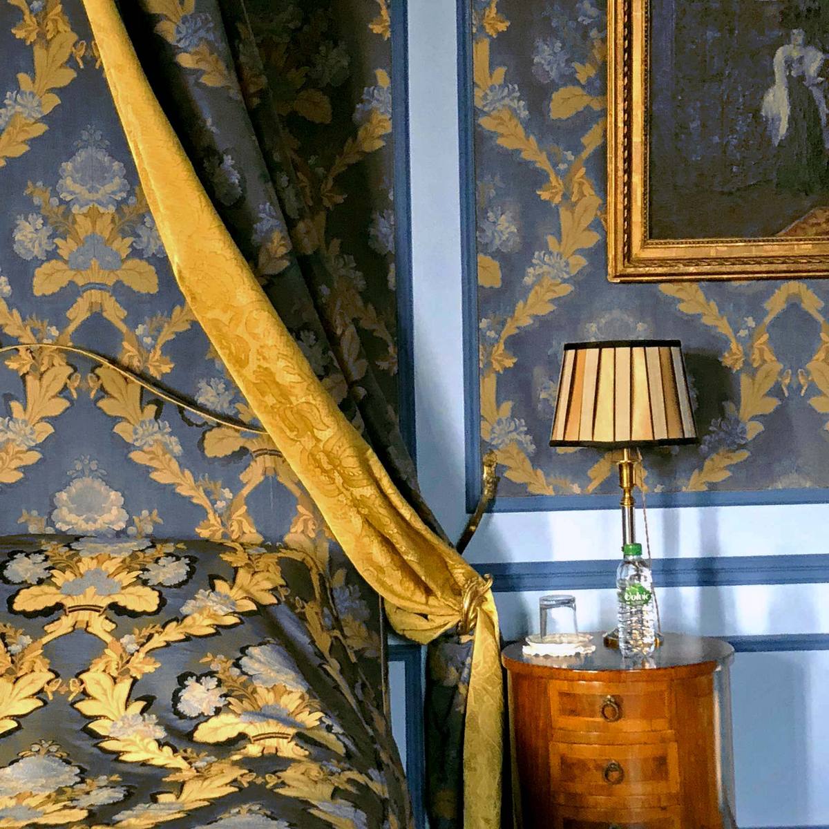 Suite Marin de Vanssay detail: gold canopy drape, bedside lamp and marquetry night table