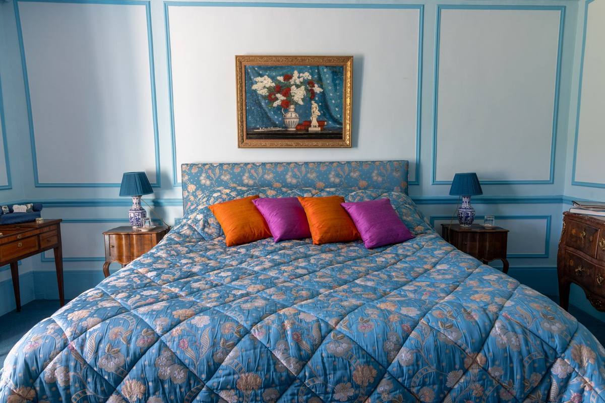 Chambre Turquoise: double bed with blue floral quilt and bright cushions, lamps on each side