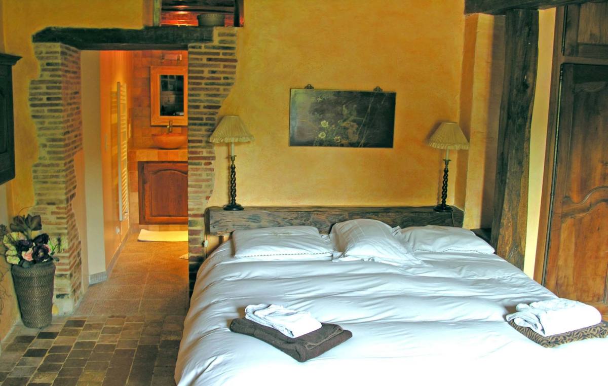Cottage Les Glycines bedroom: double bed with folded towels, bedside lamps, brick arch to the bathroom