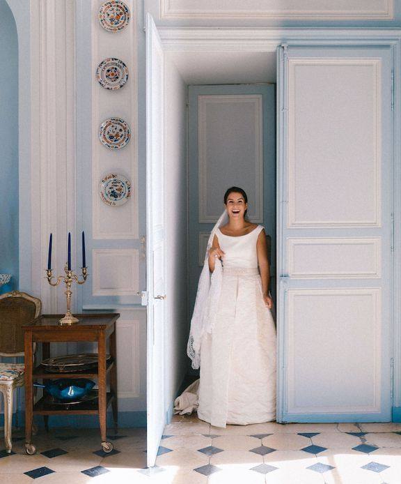 Eine lächelnde Braut im Brautkleid in einer Tür, blaue Wandvertäfelung und Schachbrettboden