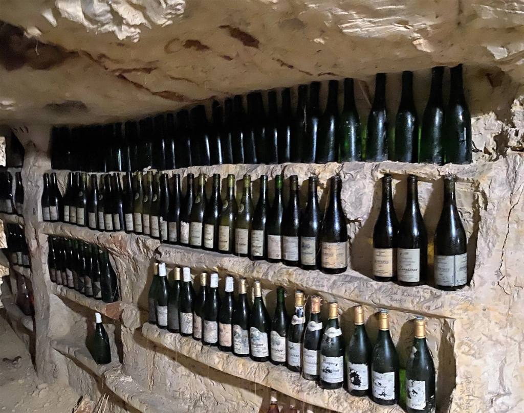 Vieilles bouteilles alignées sur des étagères taillées dans une cave de tuffeau, Jasnières