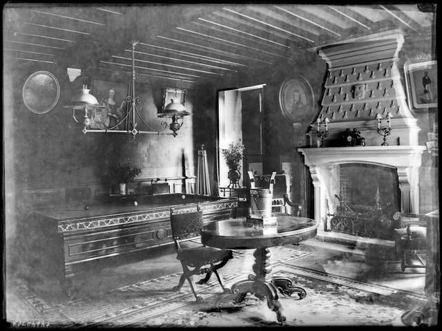 Black-and-white photograph of a salon with a monumental stone fireplace and beamed ceiling