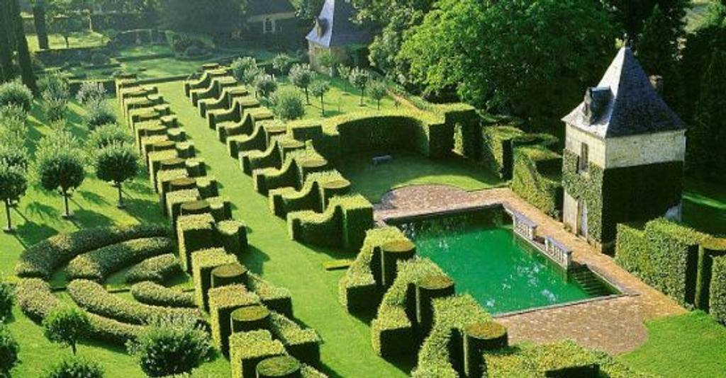 Formal garden of clipped hedges and topiary around a rectangular pool and a stone pavilion