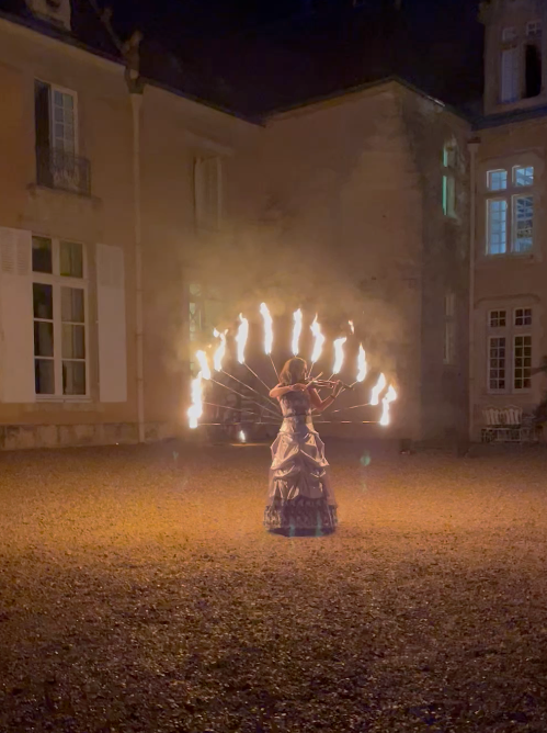 Performer in a long gown with a fan of flames at night in the château courtyard