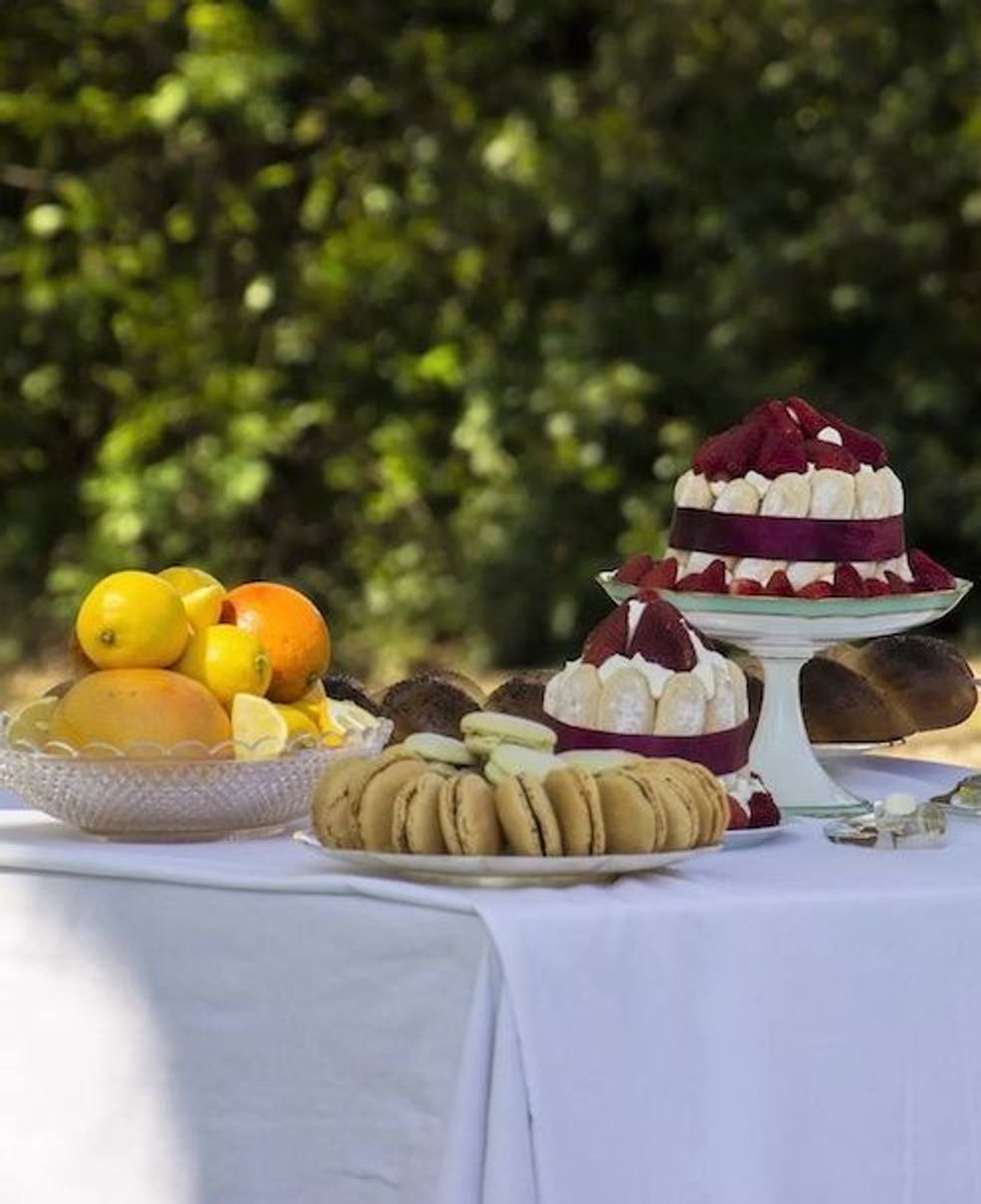 Charlottes aux fraises, biscuits et coupe d'agrumes sur une table nappée de blanc au jardin