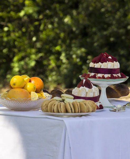 Strawberry charlottes, biscuits and a bowl of citrus fruit on a white-clothed table in the garden