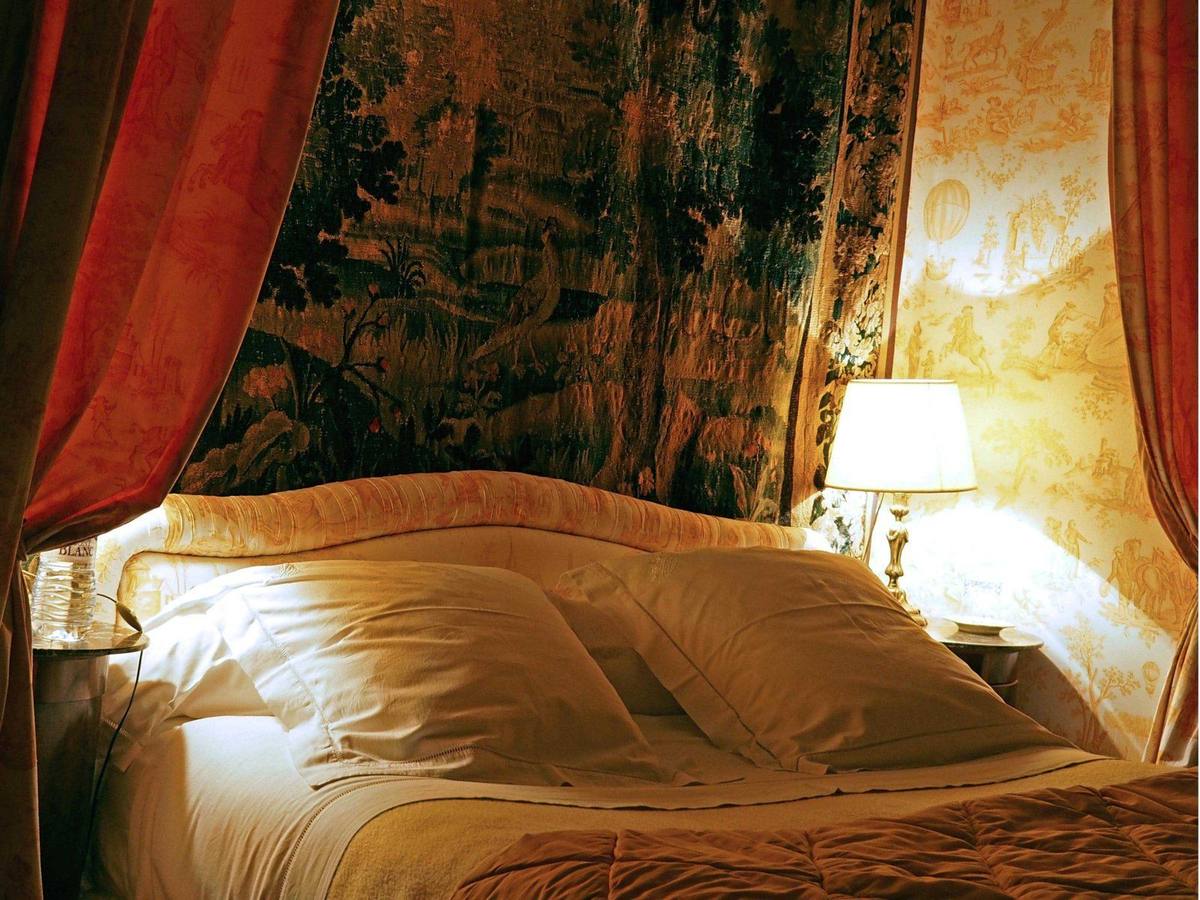 Chambre Jaune: bed with plump pillows beneath a tapestry, lit by a bedside lamp
