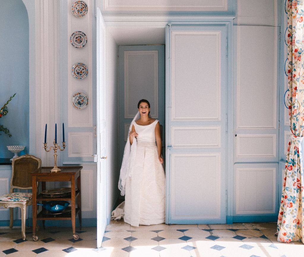 Bride in a white gown standing in a doorway of a pale blue panelled room