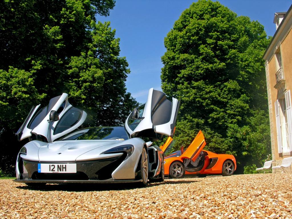 Supercars argentée et orange, portes relevées, garées sur le gravier devant le château