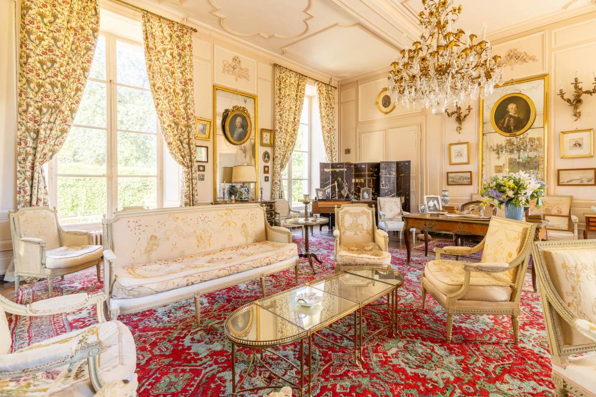 Grand Salon: pale sofa and armchairs on a red carpet, crystal chandelier and portraits on the walls