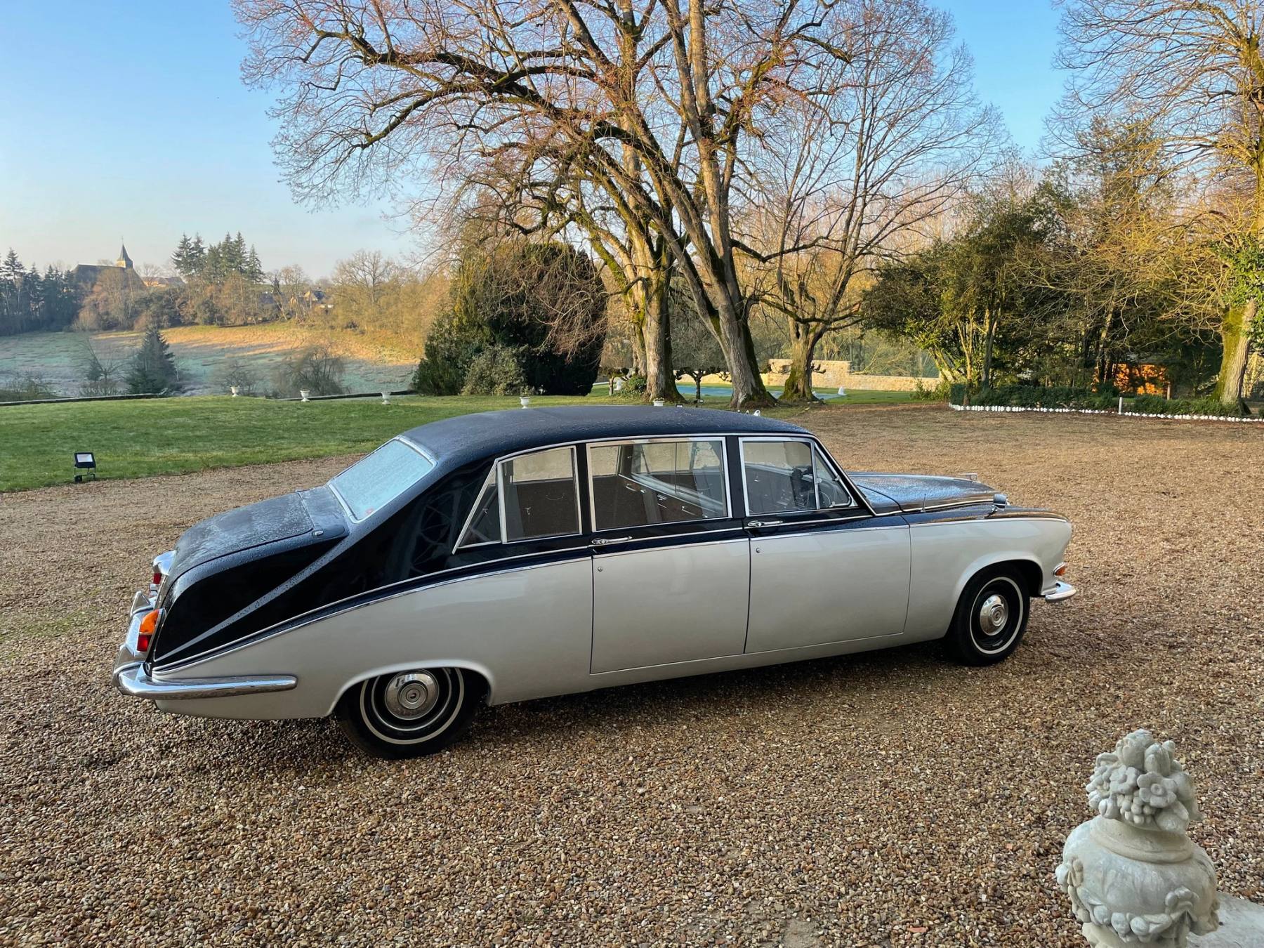 Dunkelblau-silberne Oldtimer-Limousine auf dem Kiesvorplatz, dahinter Park und Bäume