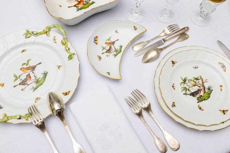 Tisch von oben: Herend-Porzellan mit Vogeldekor, Halbmondteller, Silberbesteck und bestickte Serviette