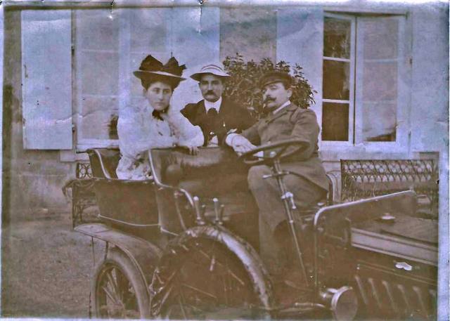 Old photograph of three people in hats seated in an early motor car before the château