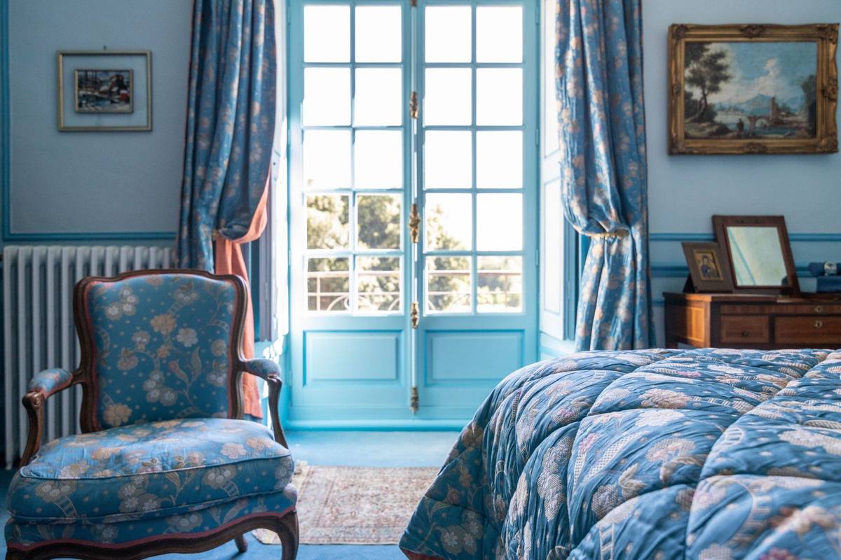 Chambre Turquoise: blue floral cabriolet armchair beside a French window and the bed