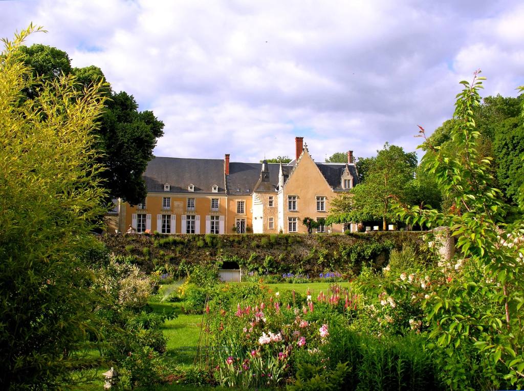 The château façade seen from the garden, beyond flowering borders, roses and a clipped hedge