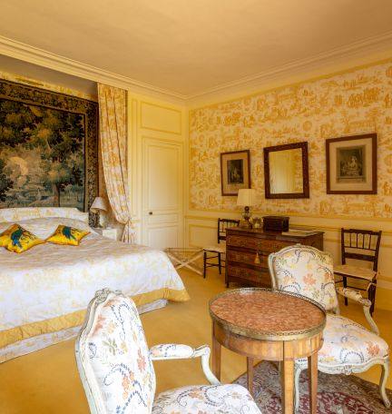 Chambre Jaune: bed below a verdure tapestry, yellow toile walls, guéridon and floral armchairs