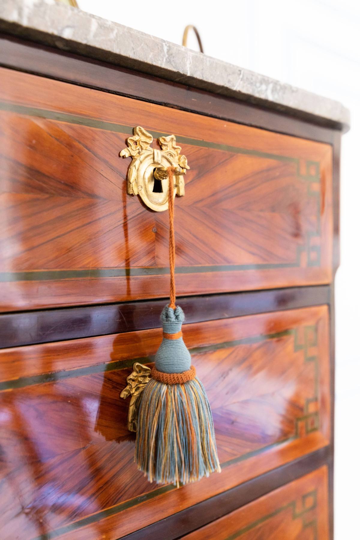 Detail of a marquetry chest of drawers with a gilt keyhole and blue silk tassel