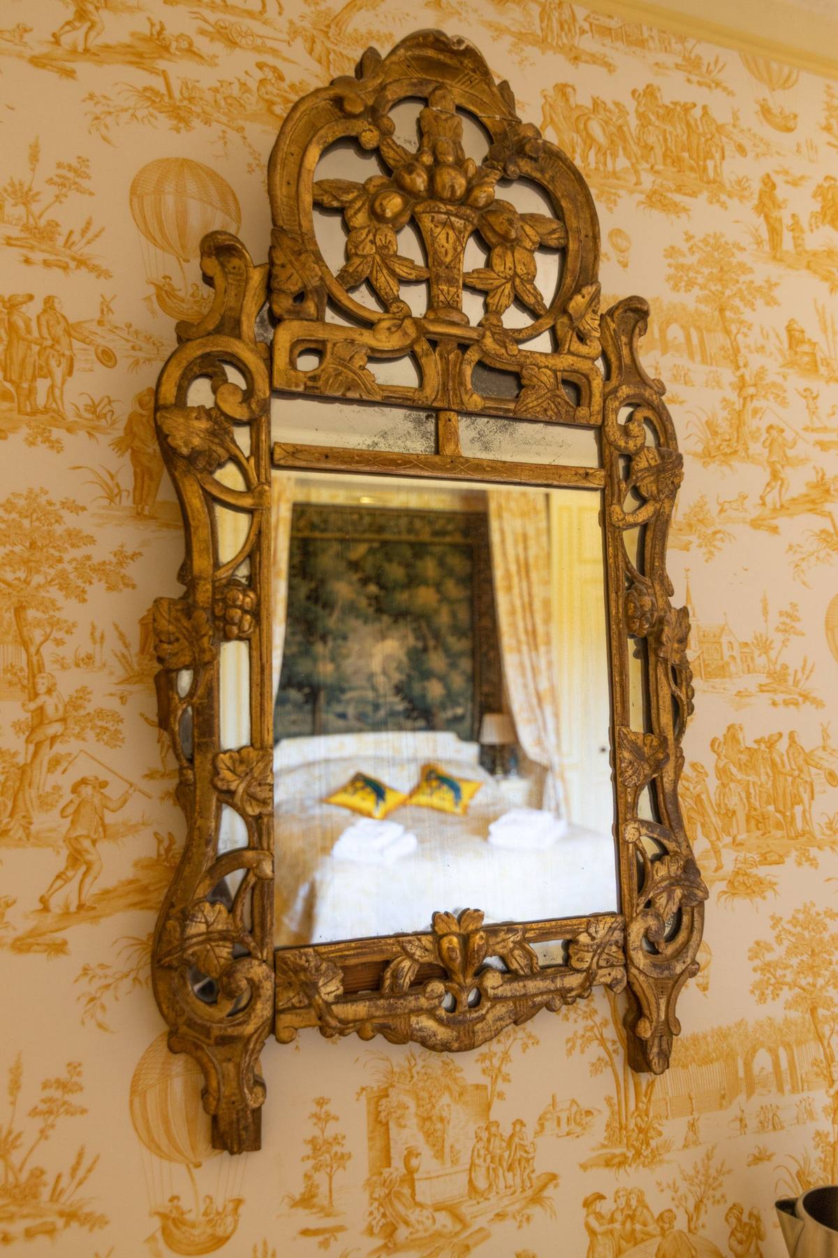 Chambre Jaune: carved gilt mirror on a yellow toile wall, reflecting the bed and tapestry