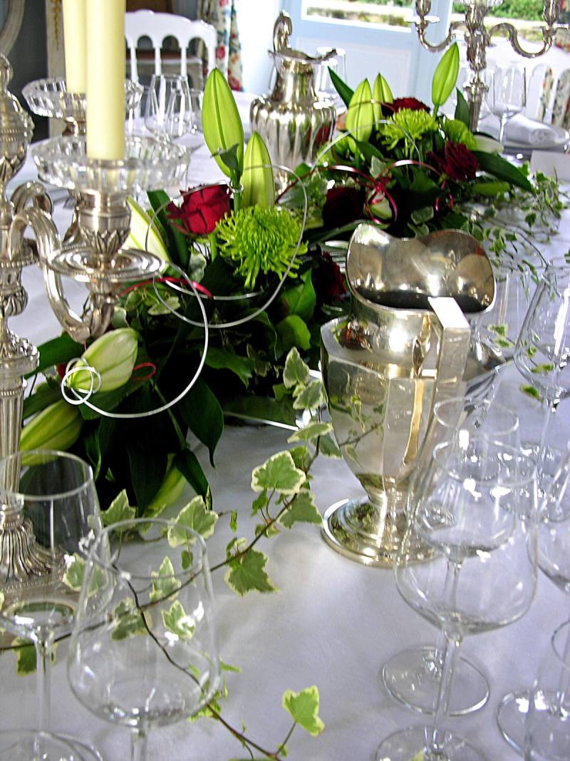 Wedding table centrepiece of lilies, roses and ivy between silver candelabra and a silver jug