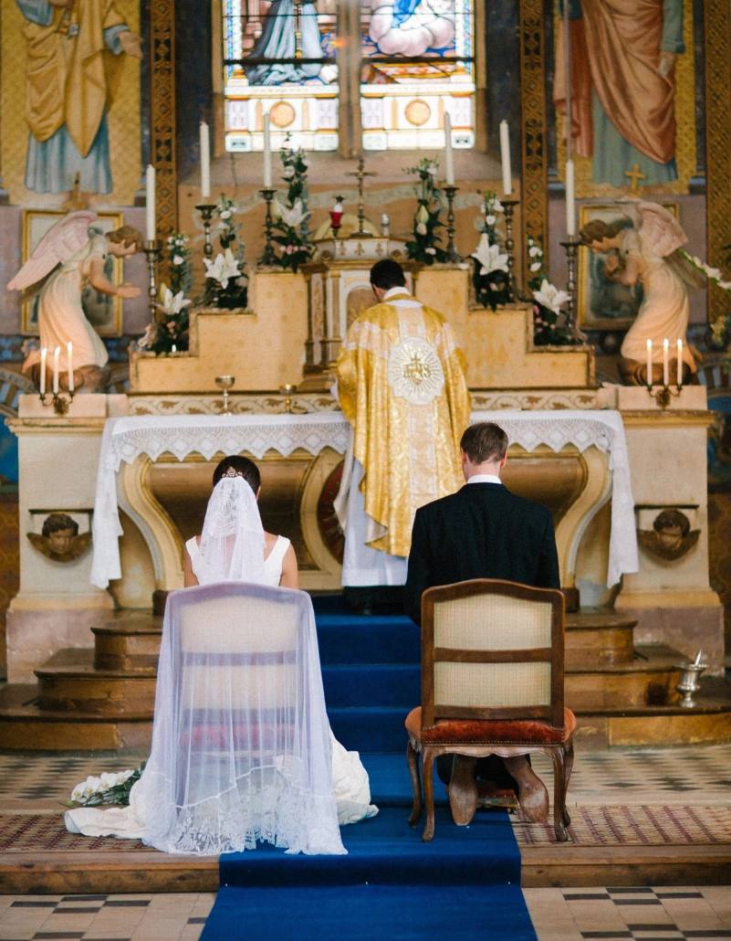 Bride and groom kneeling before the altar during the wedding mass, the priest in a gold chasuble