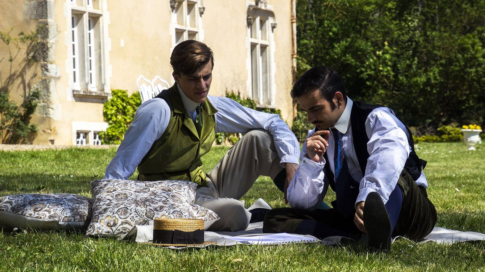 Two men in period costume picnicking on the lawn in front of the château during filming