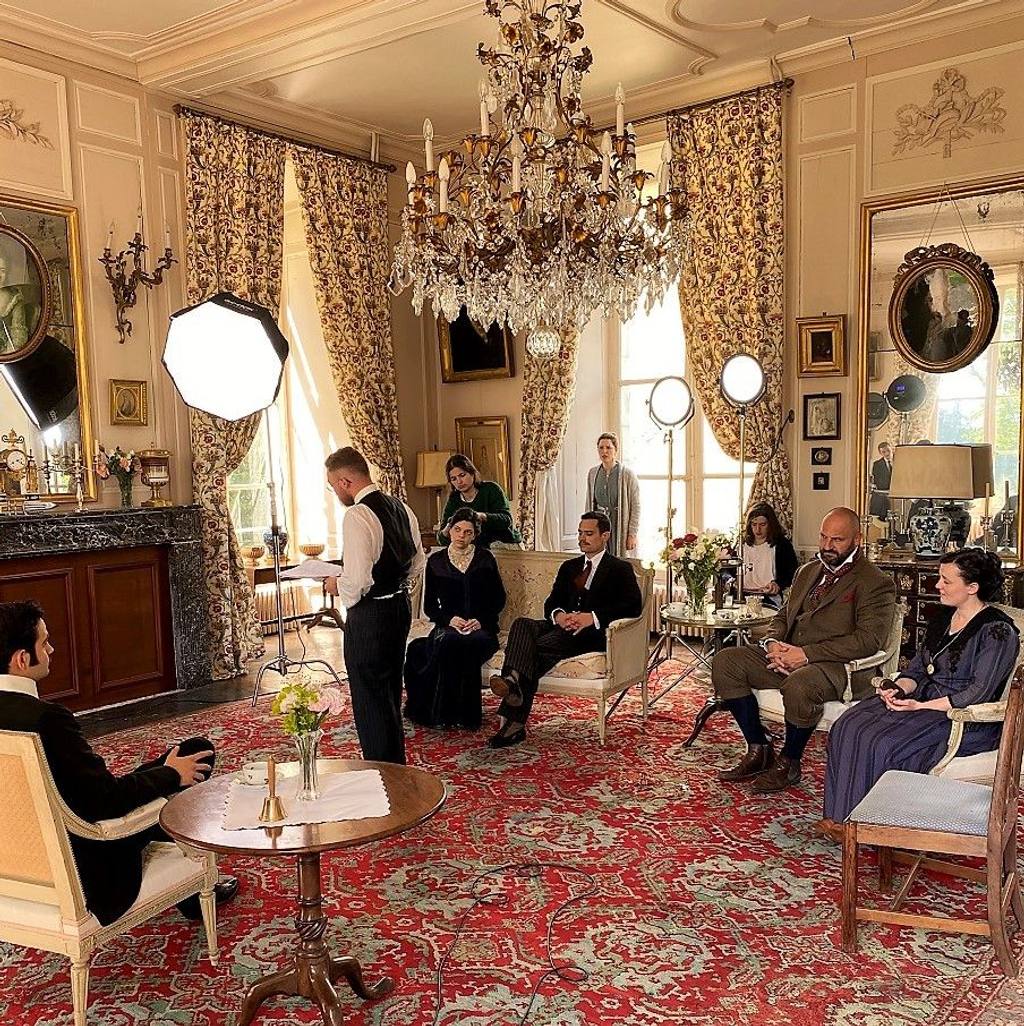 Guests in period costume in the Grand Salon beneath a crystal chandelier, with photo studio lights