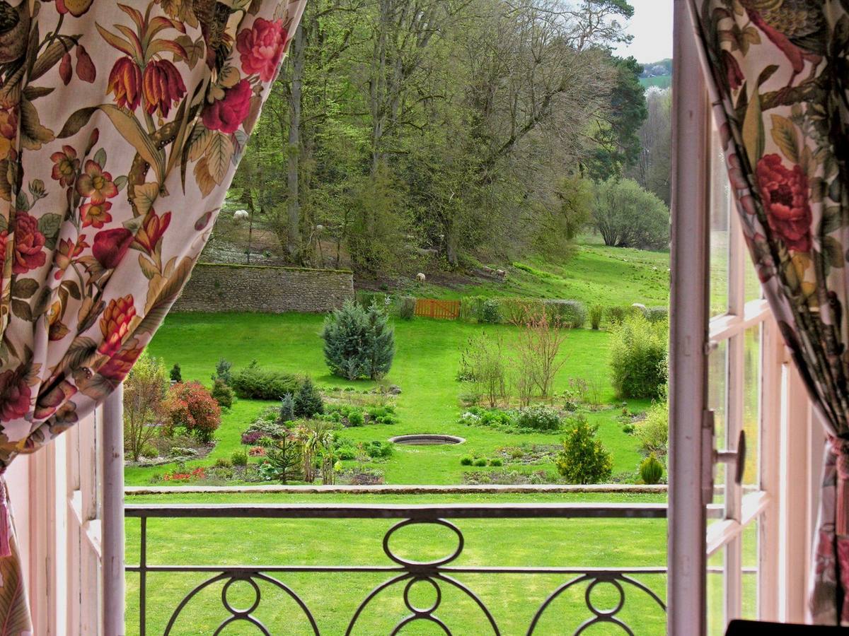 Garden view through the open window of the Oiseaux room, framed by floral chintz curtains