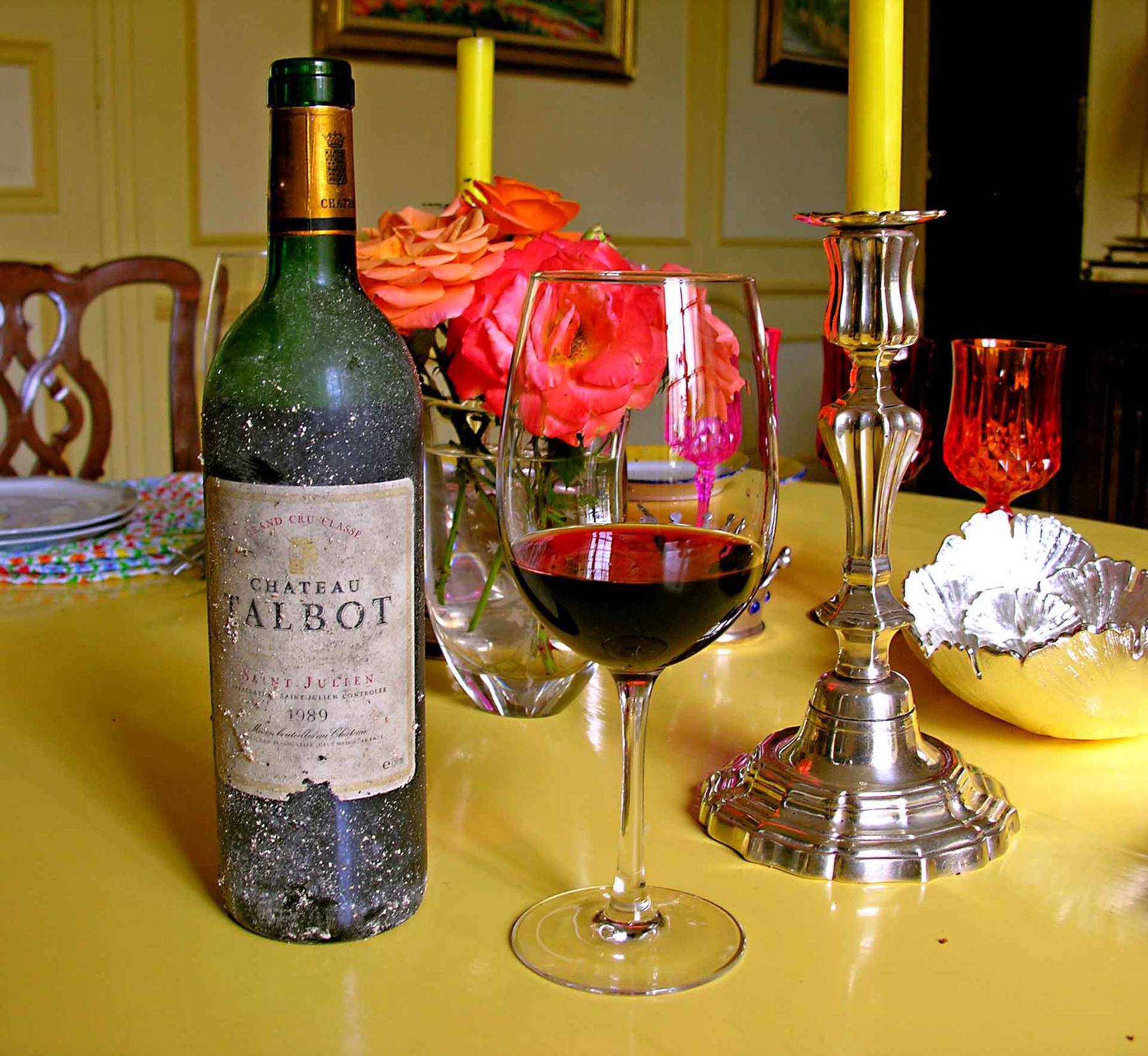 Staubige Flasche Château Talbot neben einem Glas Rotwein, Rosen und einem silbernen Kerzenleuchter