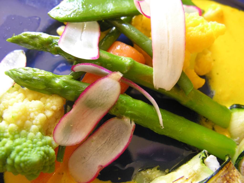 Close-up of spring vegetables: asparagus, romanesco, snow peas and shaved radish on a golden sauce