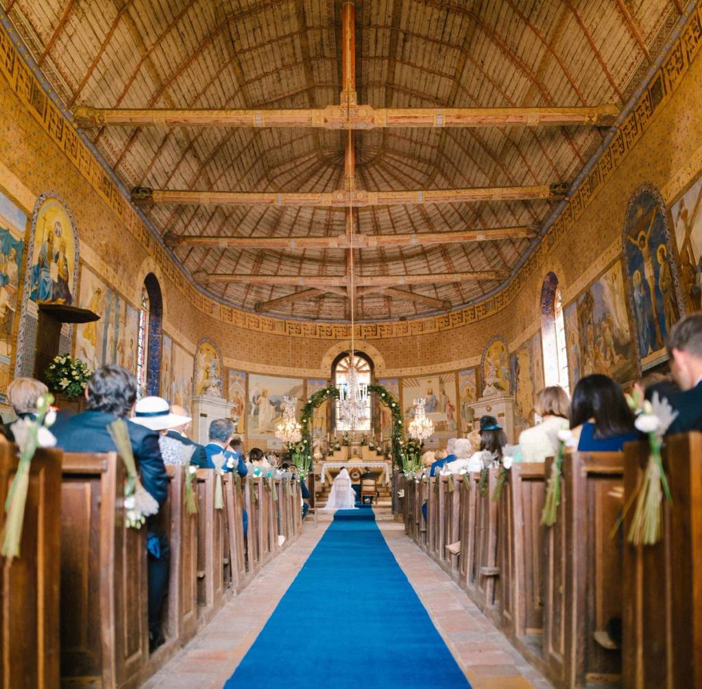 Wedding ceremony in a church with painted walls, a blue aisle carpet and guests in the pews