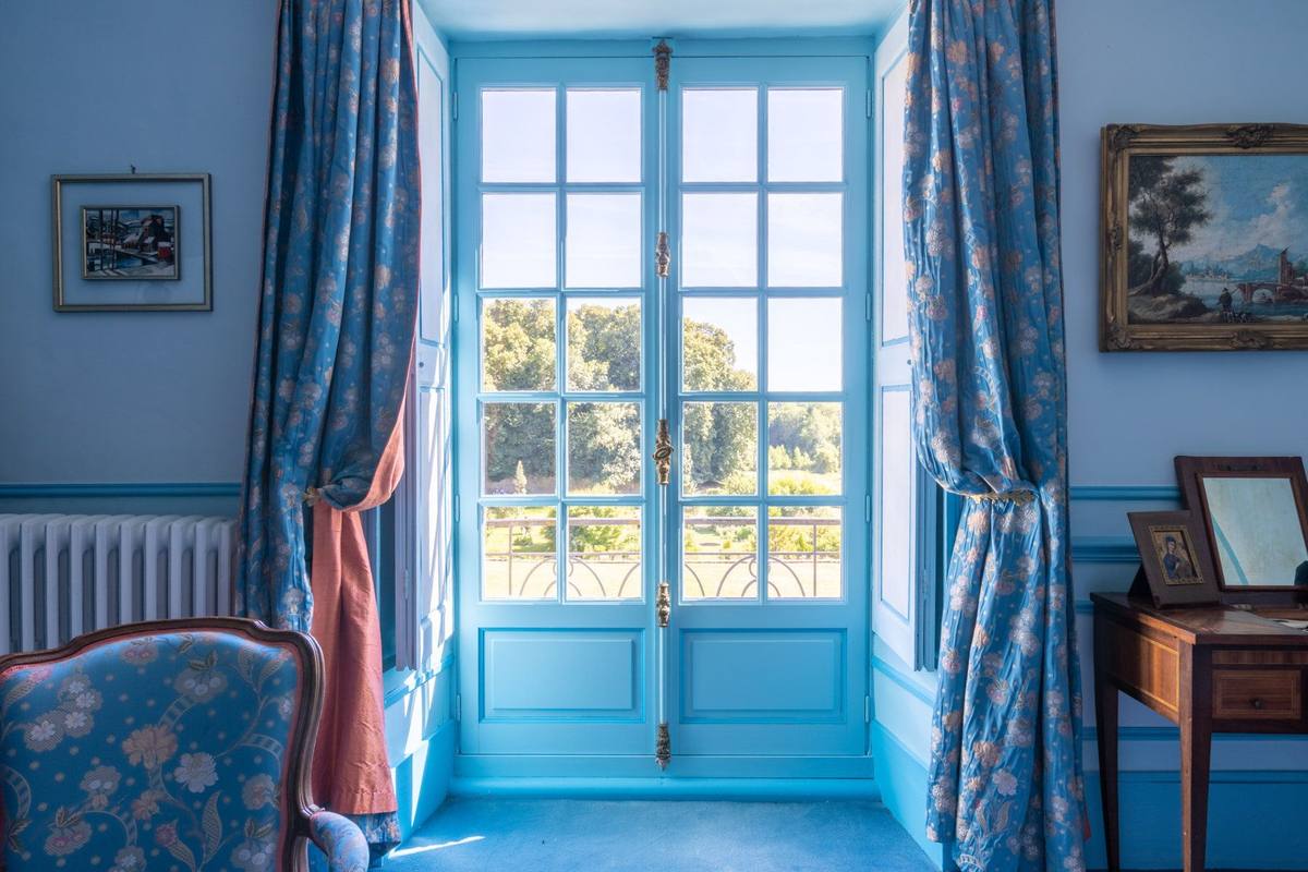 Chambre Turquoise: French window with blue floral curtains opening onto a balcony and the park