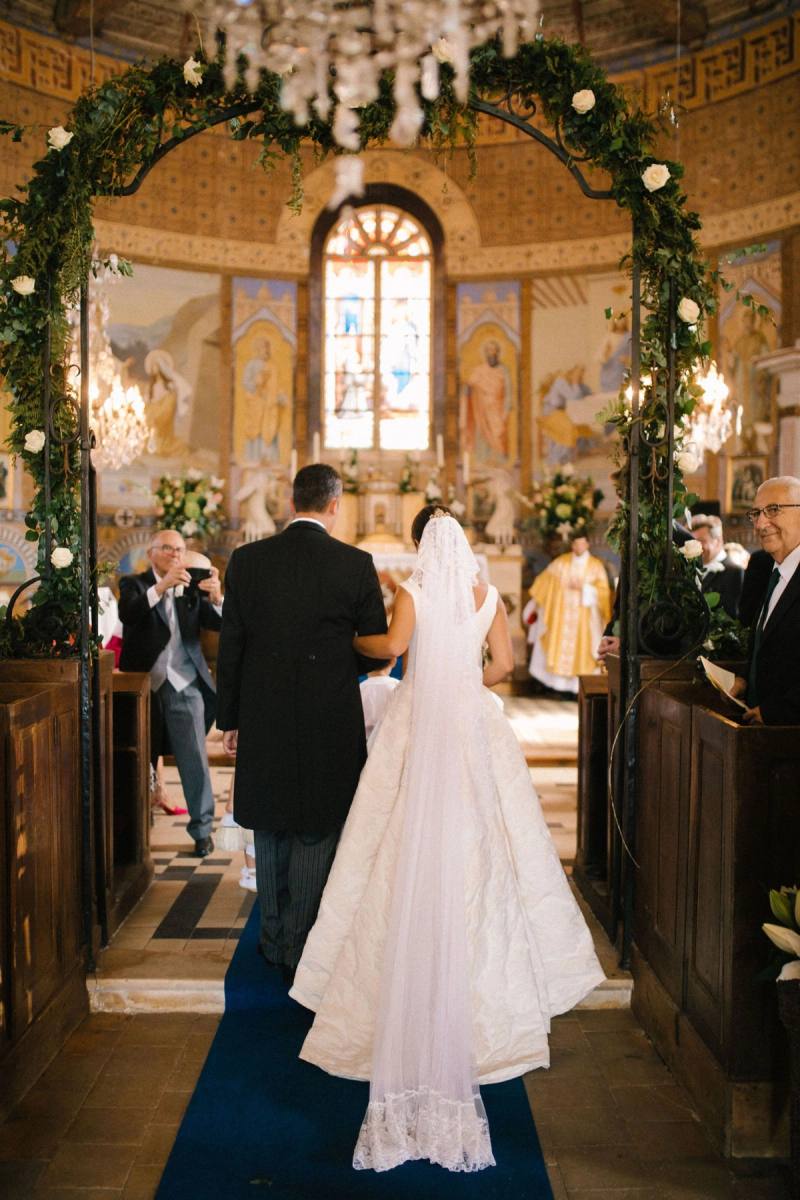 Bride and groom at the altar under an arch of white roses, guests in the pews of a painted church