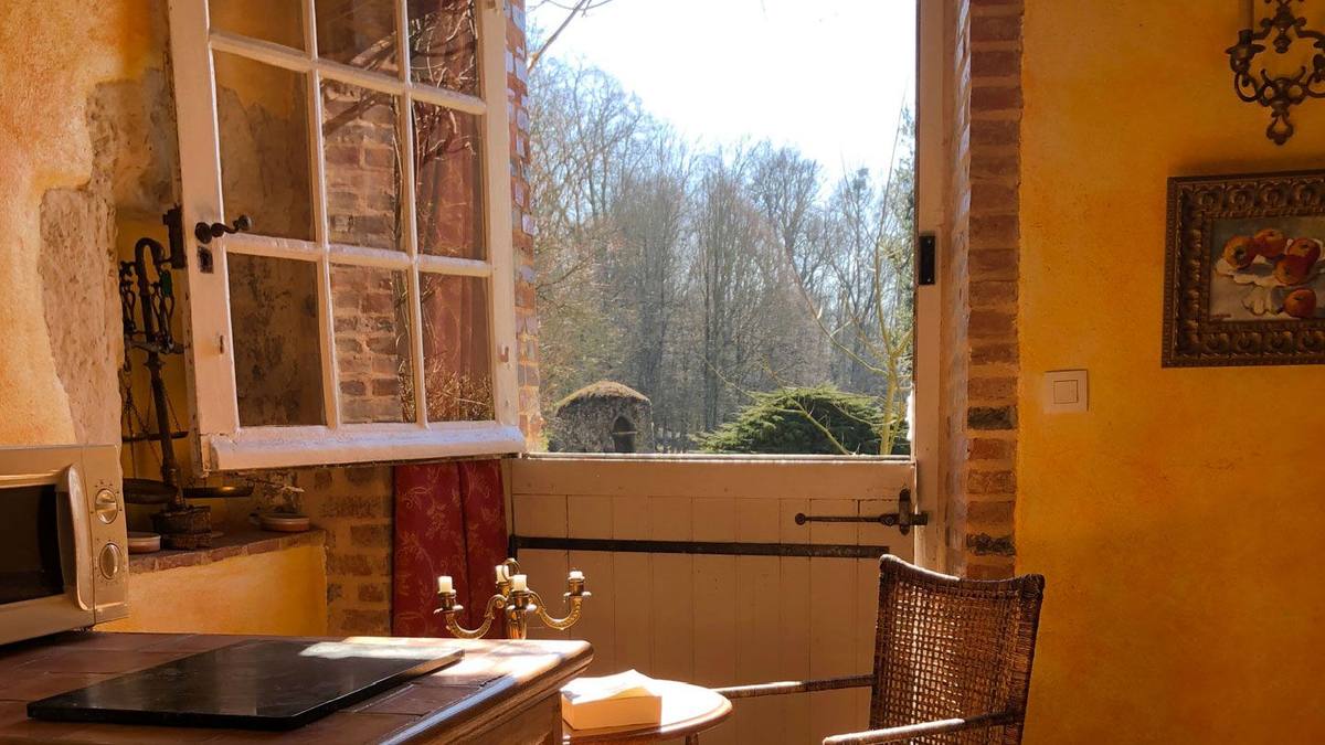 Open window of Cottage Les Glycines looking onto the garden, with hob, candlestick and wicker chair