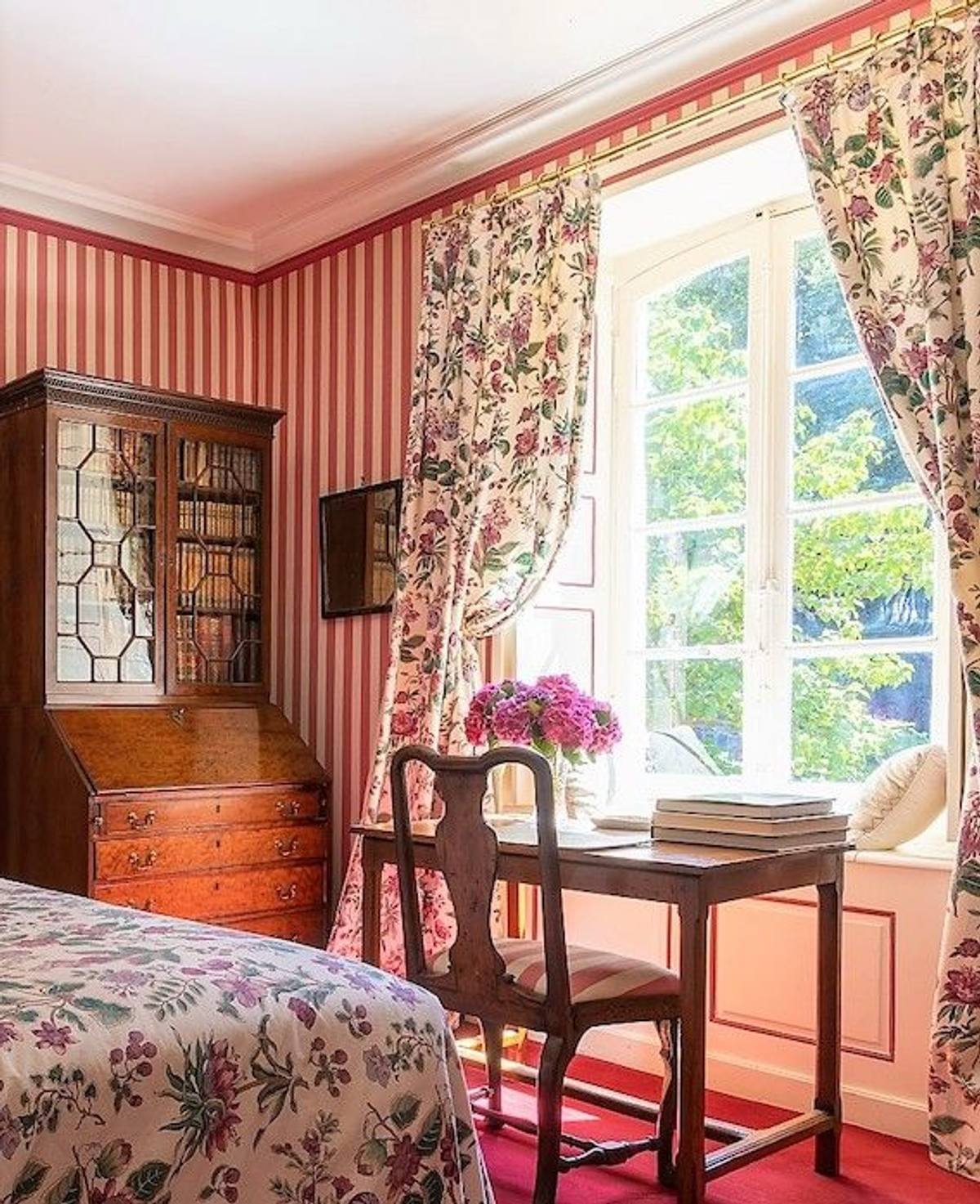 Chambre aux Fleurs: desk before a tall window with floral curtains, beside a glazed secretary bookcase