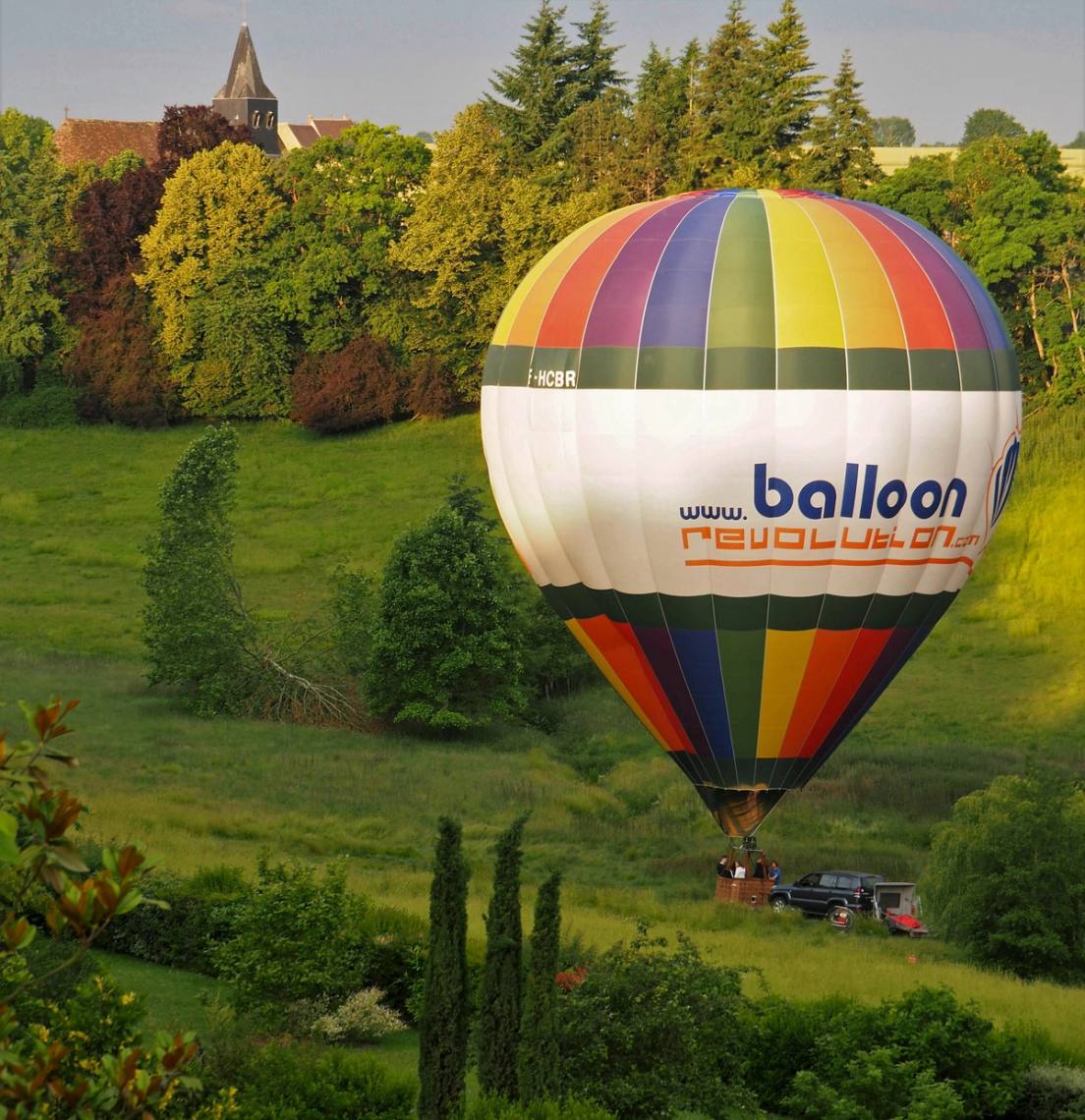 Montgolfière aux bandes arc-en-ciel flottant au ras de la campagne verdoyante, dans la lumière du soir