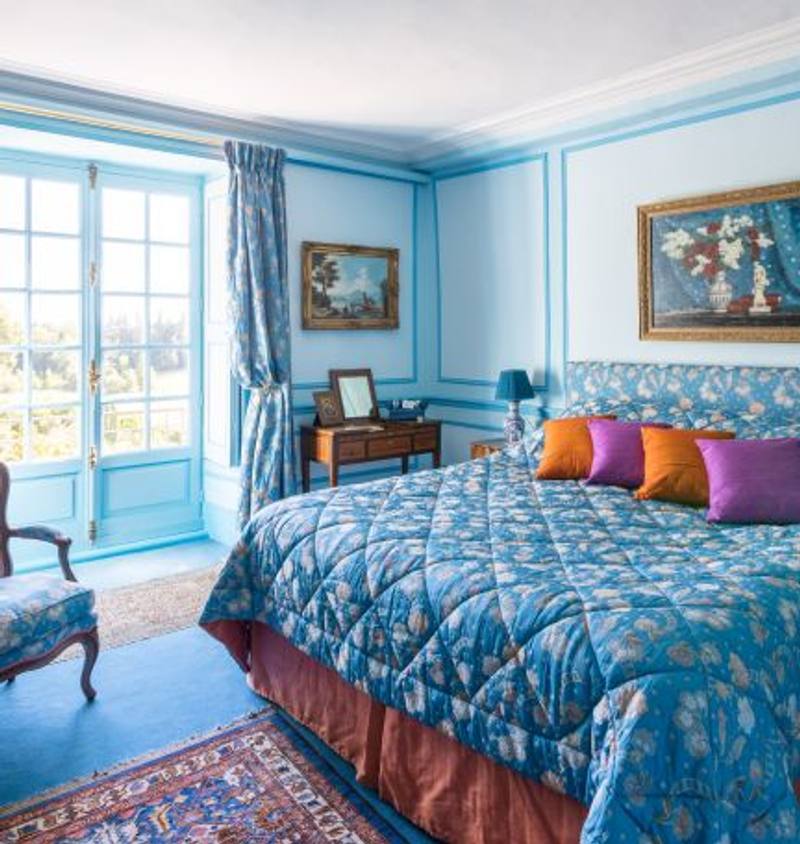 Chambre Turquoise: blue quilted bed with orange and purple cushions, French window onto the park