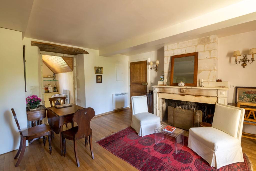 Gîte Les Lilas: sitting room with stone fireplace, two white armchairs and a red rug
