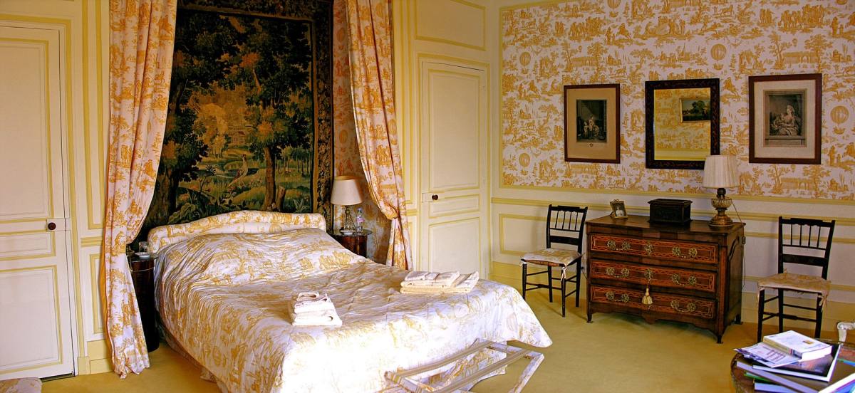 Chambre Jaune: wide view of the bed beneath a tapestry, chest of drawers and yellow toile walls