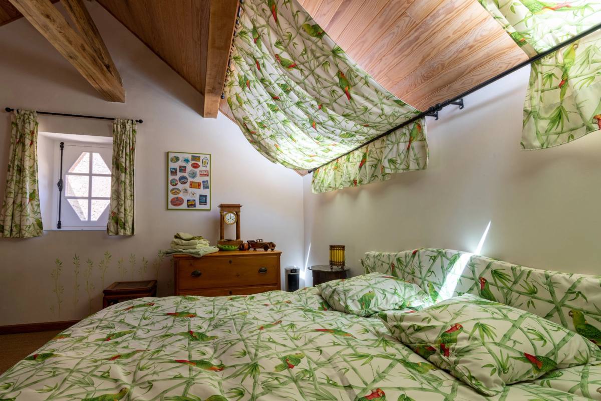 Gîte Les Lilas: upstairs double bed under a sloping wooden ceiling, leaf-print fabrics