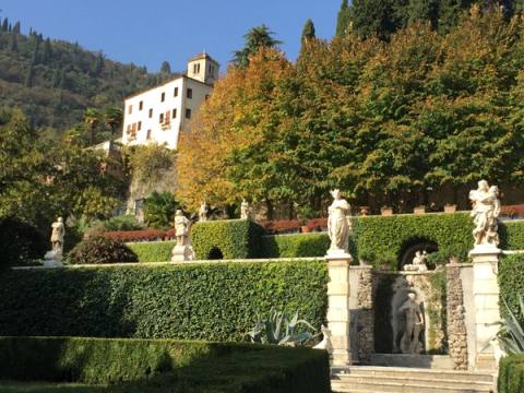 Terraced Italianate garden with clipped hedges and statues below a hillside villa in autumn