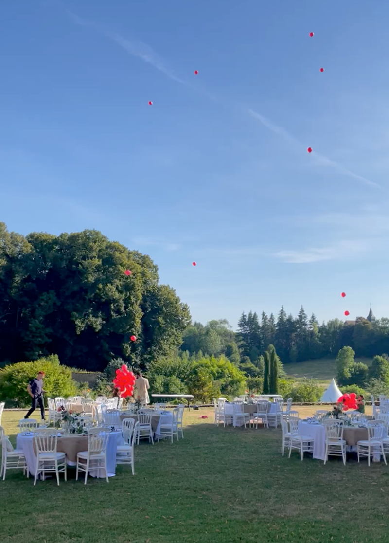 Red balloons released above a wedding reception with tables set on the lawn