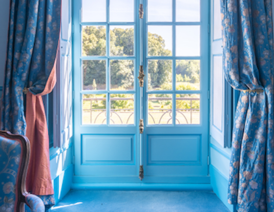 Chambre Turquoise: sunlit French doors with blue floral curtains, looking out over the park
