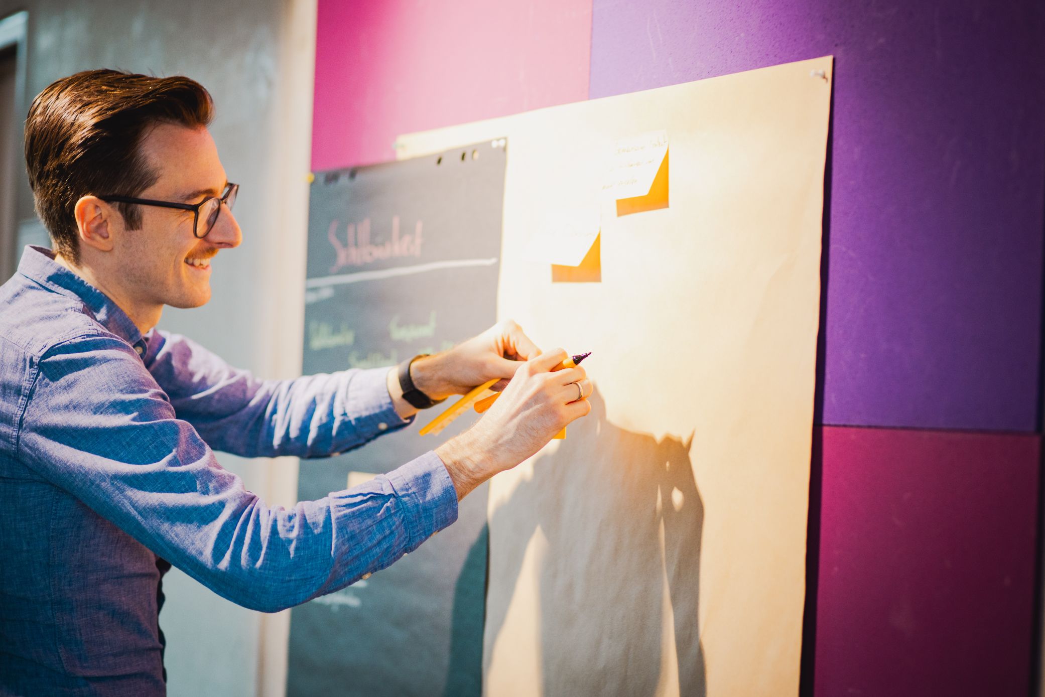 Workshop-Szene mit Kollege, der Haftnotizen an eine Wand hängt – partizipativer Start individueller Softwareprojekte