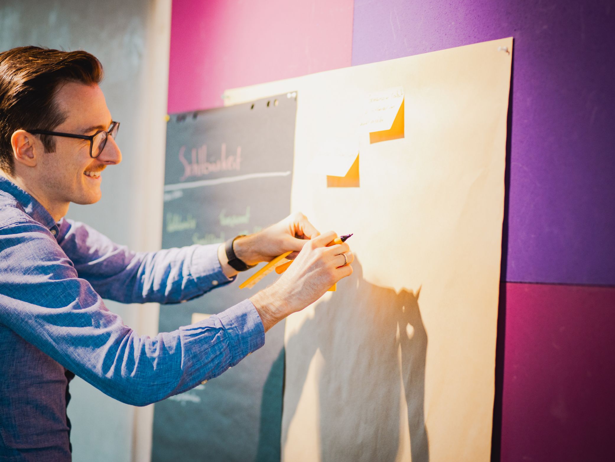 Individueller Startpunkt in der Softwareentwicklung: Anforderungen im Team sichtbar machen Workshop-Szene mit Kollege, der Haftnotizen an eine Wand hängt – partizipativer Start individueller Softwareprojekte